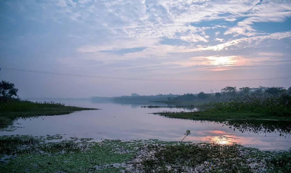 A still lake at sunrise under a sky of thin pink and blue cloud